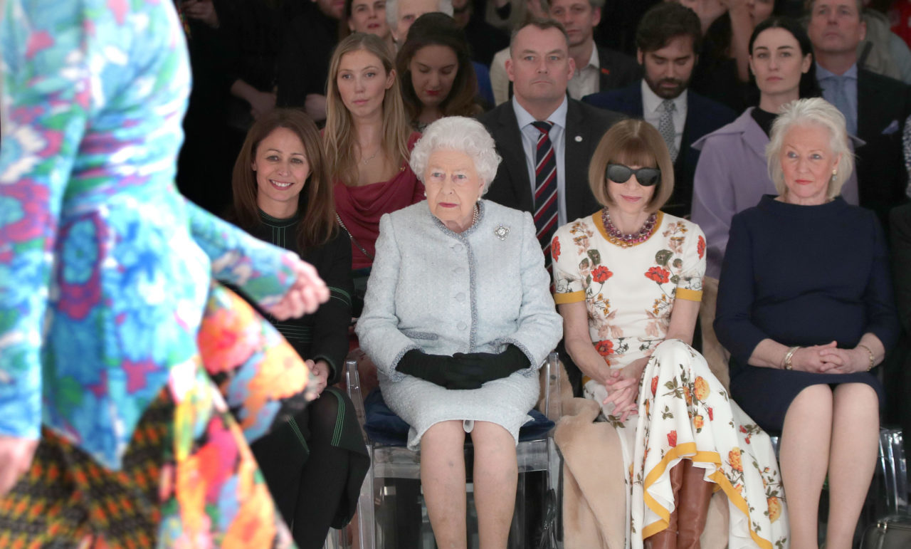 LONDON, ENGLAND - FEBRUARY 20: Queen Elizabeth II sits with American Vogue editor Anna Wintour, Caroline Rush (L), chief executive of the British Fashion Council (BFC) and royal dressmaker Angela Kelly (R) as they view Richard Quinn's runway show before presenting him with the inaugural Queen Elizabeth II Award for British Design as she visits London Fashion Week's BFC Show Space on February 20, 2018 in London, United Kingdom.