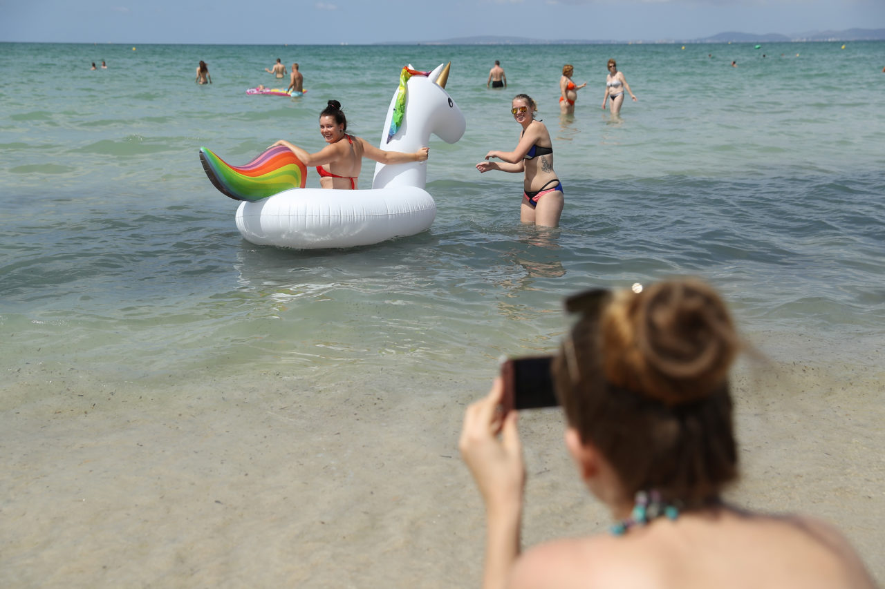 PALMA DE MALLORCA, SPAIN - JULY 26: Female visitors bring an inflatable beach mattress in the shape of a unicorn to the water at the beach along the Ballermann stretch on July 26, 2017 in Palma de Mallorca, Spain. The term Ballermann, which combines the Spanish word for bathing site "balneario" and the German slang word for heavy drinking "ballern," has become synonymous with the party atmosphere of the beach-front street. The stretch is especially popular among young German and Dutch tourists, who spend the days at the beach and the nights in the pubs and discos. (Photo by Sean Gallup/Getty Images)